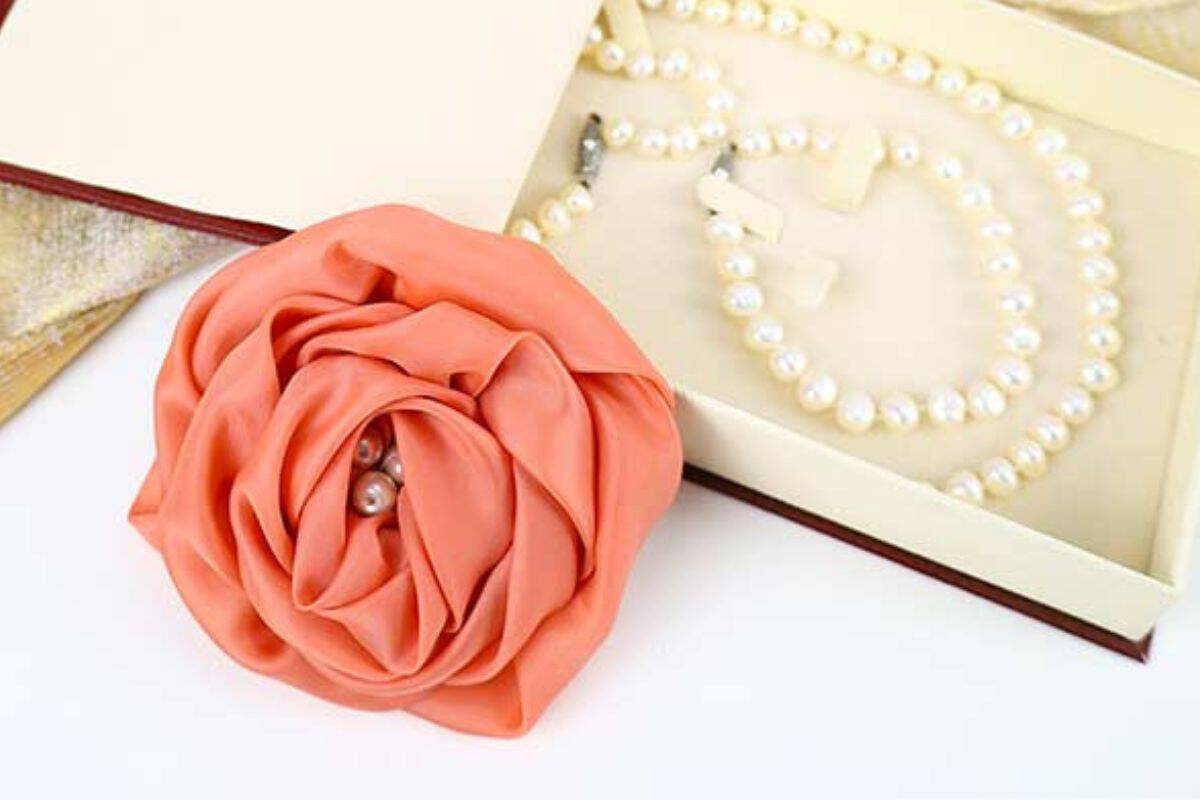 Handcrafted fabric rose with layered petals and pearl embellishments positioned beside an open jewelry case containing a pearl necklace and earrings.