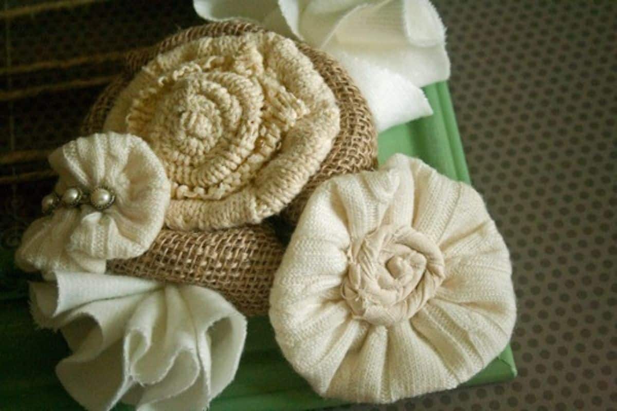 Handcrafted fabric flowers made from burlap and sweater material, layered and arranged as rustic floral ornaments on a wrapped present.