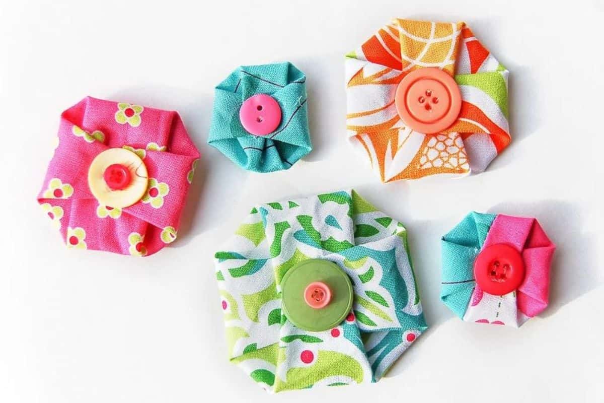 Various handmade no-sew fabric flowers in assorted sizes and patterns, each folded into a rosette style and completed with a button centerpiece.