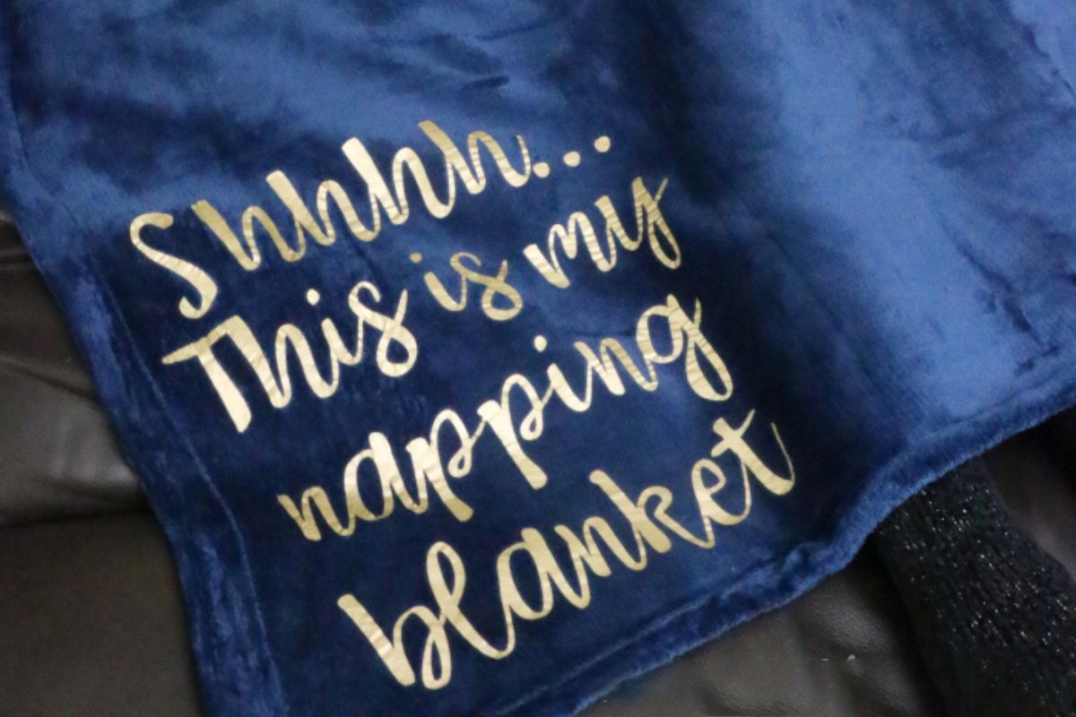 A plush navy blue blanket with gold text stating 'Shhhh... This is my napping blanket,' elegantly displayed over a surface, exuding a warm and inviting atmosphere.