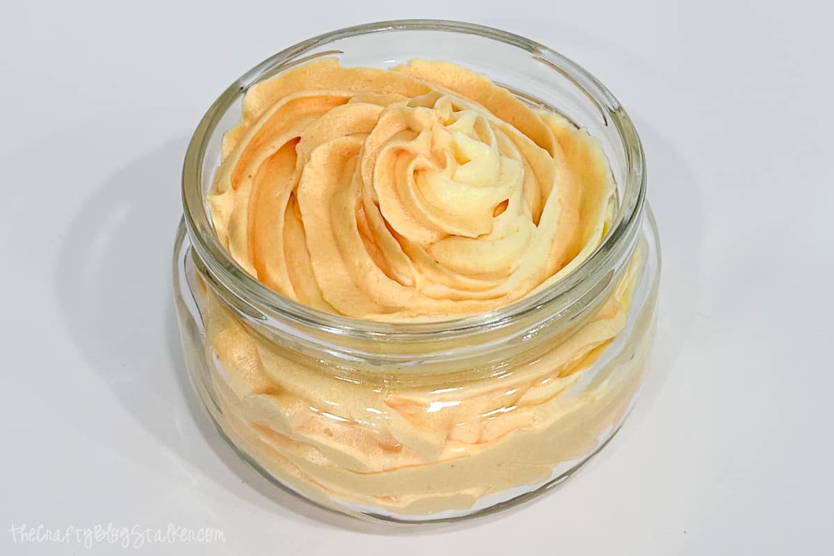A glass container filled with exfoliating whipped soap.