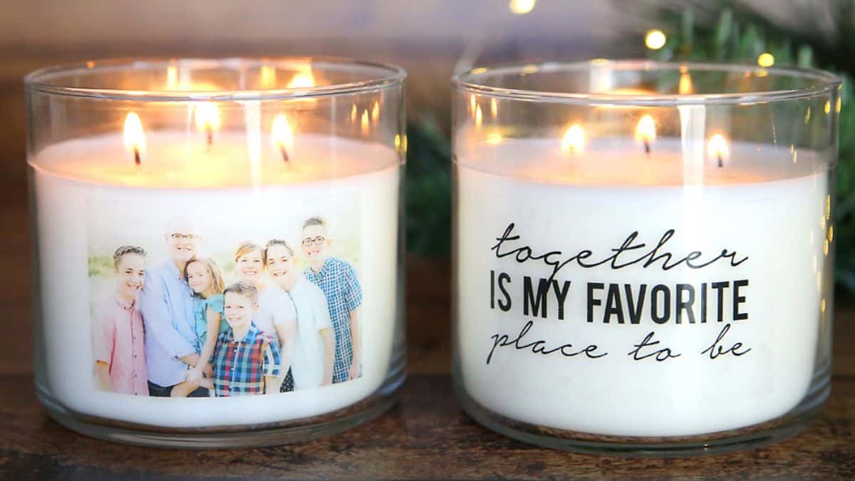 Two illuminated glass jar candles on a surface, one adorned with a family picture and the other featuring a handwritten-style quotation, arranged side by side.