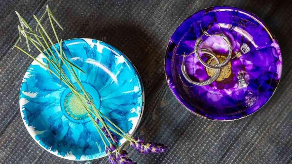 Two circular handmade jewelry bowls embellished with alcohol ink designs, one containing lavender sprigs and the other holding rings and earrings.