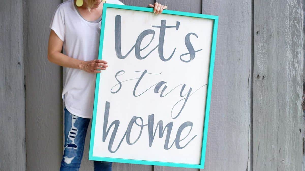 Individual holding a large framed wooden sign with a handwritten quote, posed in front of a weathered wood backdrop.