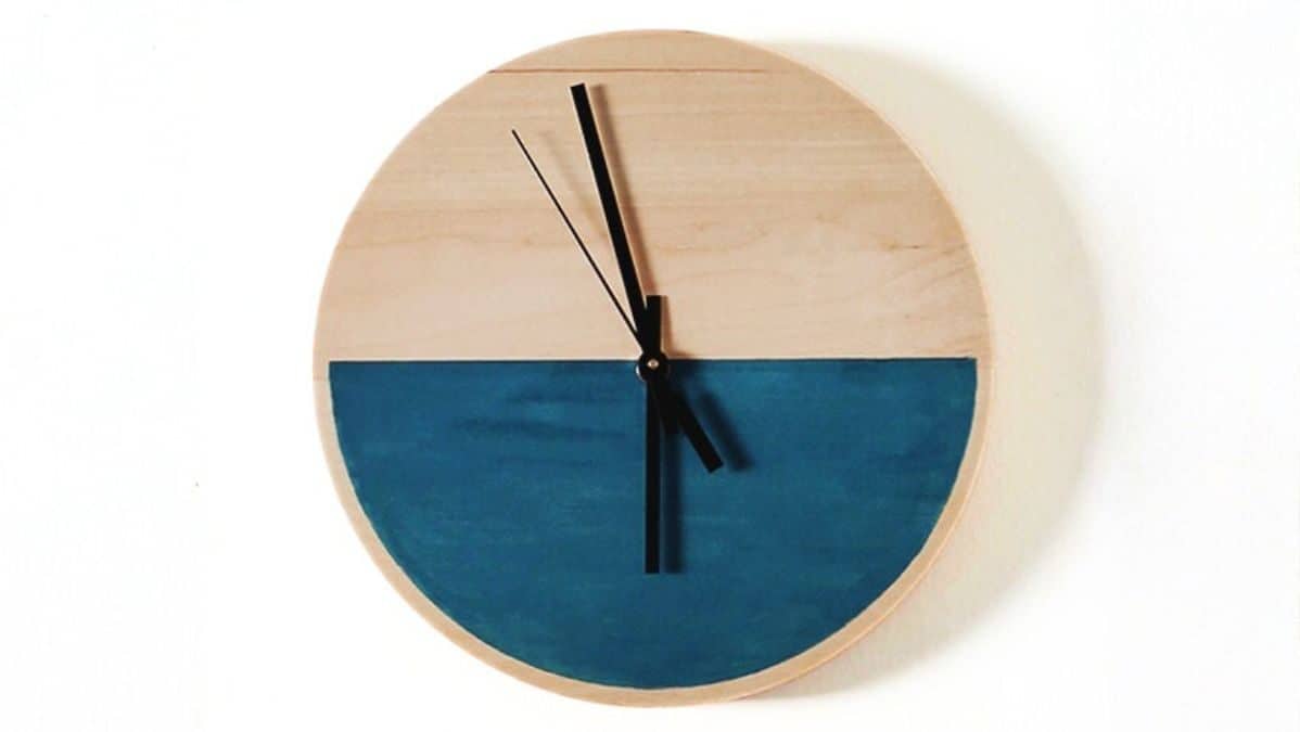 Round wooden wall clock with a painted bottom half and black clock hands against a simple background.