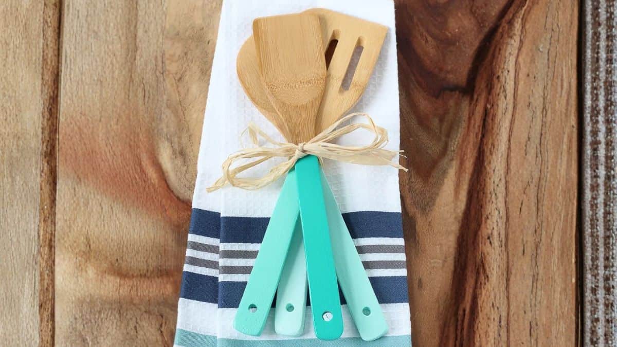 Set of bamboo kitchen tools with painted handles bundled together and showcased on a folded striped dish towel laid on a wooden table.