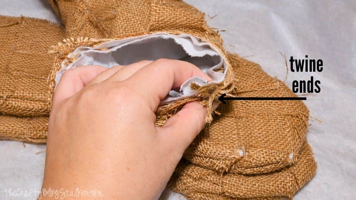 Woven Burlap Christmas Stockings Tutorial Hand grasping the cuff of a burlap stocking, displaying twine ends tucked inside the opening during the finishing step of a DIY woven burlap stocking.