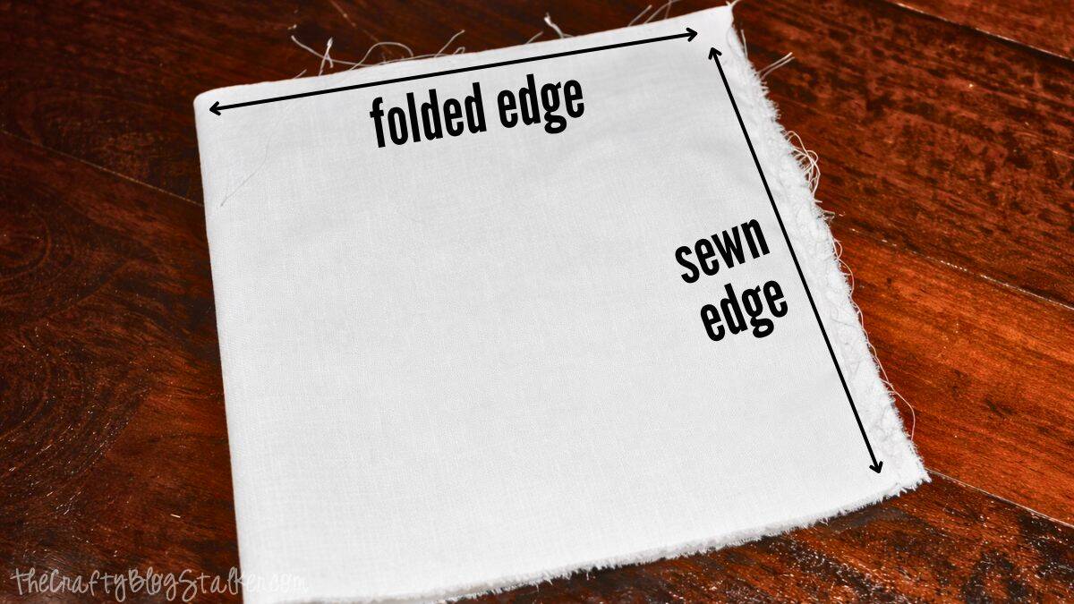 Woven Burlap Christmas Stockings Tutorial Fabric square for a stocking cuff with marked folded edge and sewn edge, displayed flat on a wooden surface as part of a step-by-step sewing guide.