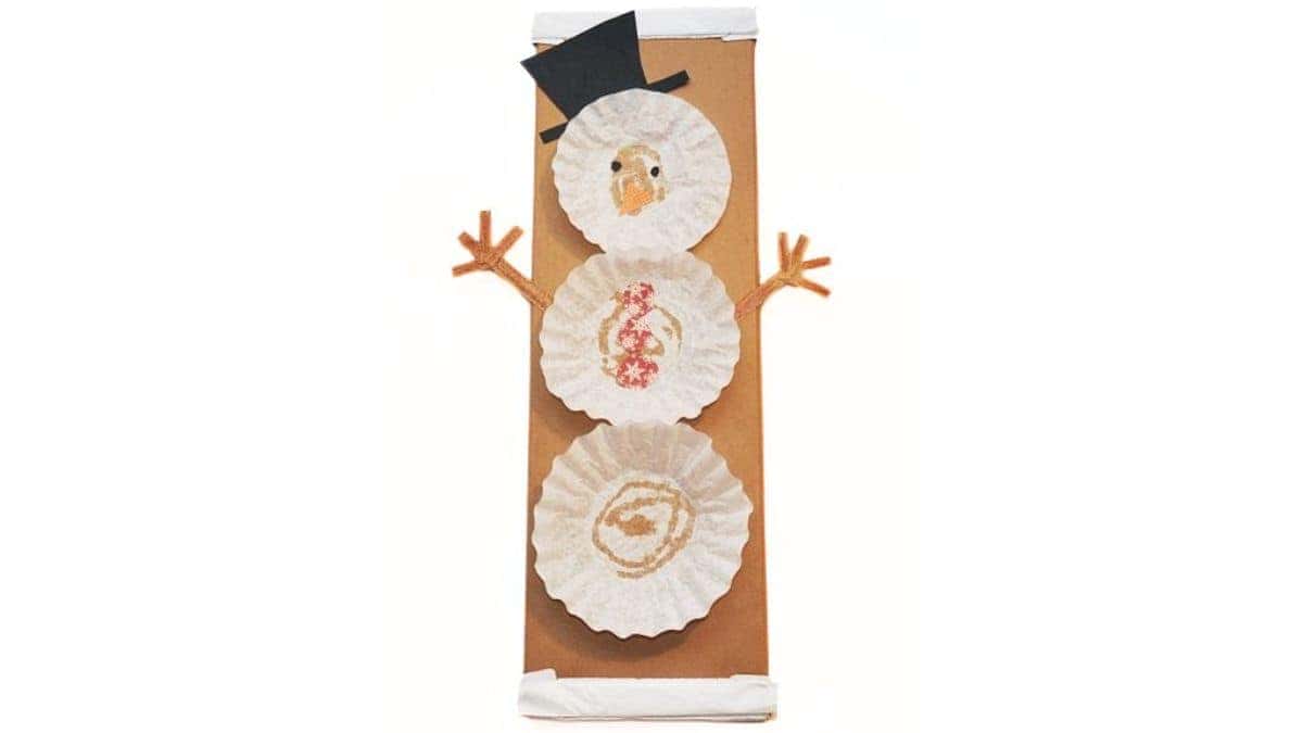 Completed coffee filter snowman craft created with stacked coffee filters, paper hat and nose, and pipe cleaner arms, attached to a brown paper gift bag.