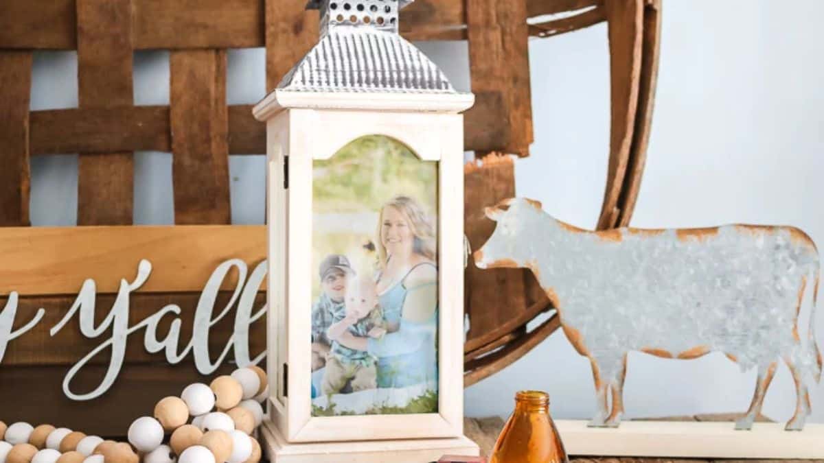 An ornamental lantern featuring a family image, arranged on a rustic shelf with wooden elements, beads, and a metal cow figurine.