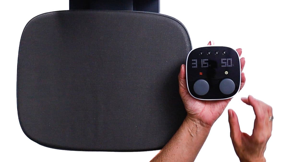 Hand grasping a heat press control panel next to a heat press platen, displaying temperature and time settings prepared for applying iron-on vinyl.