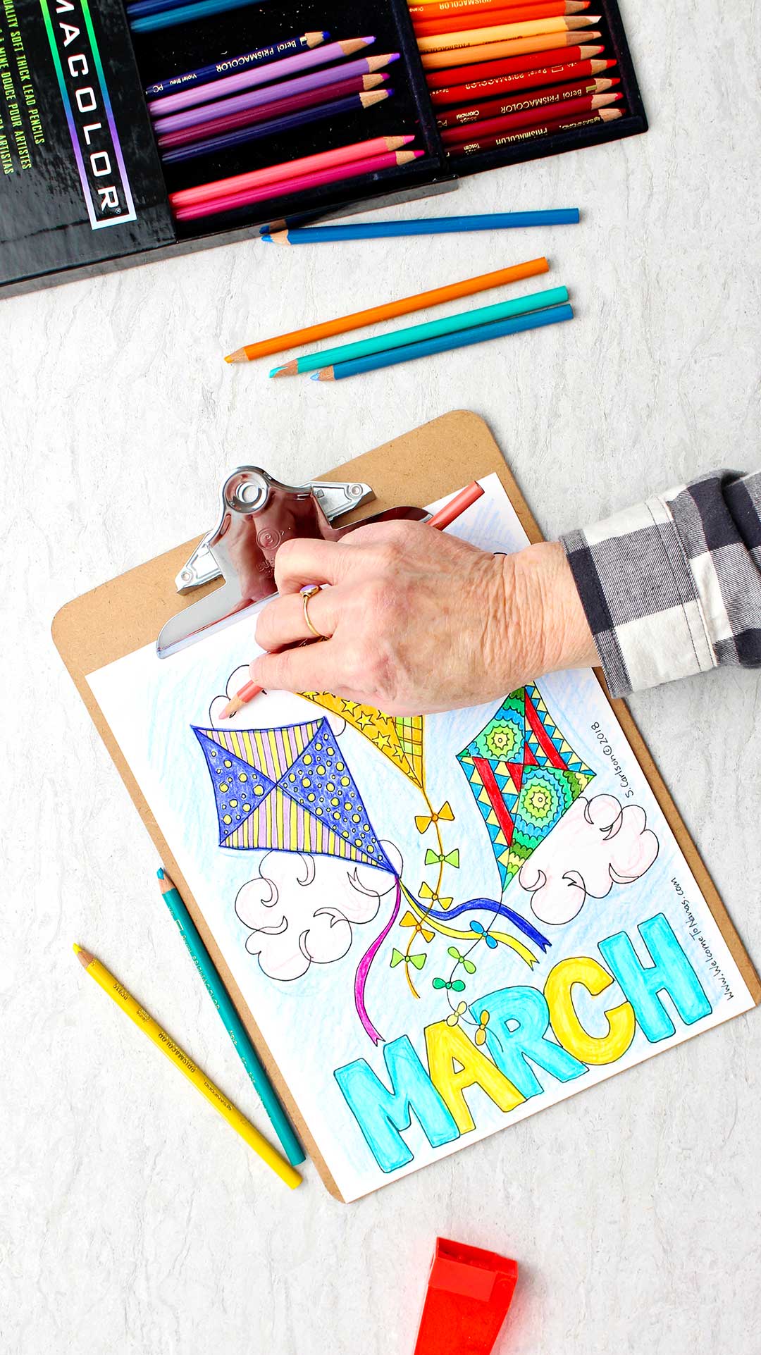 Hand using side of colored pencil to lightly shade some clouds on coloring page.