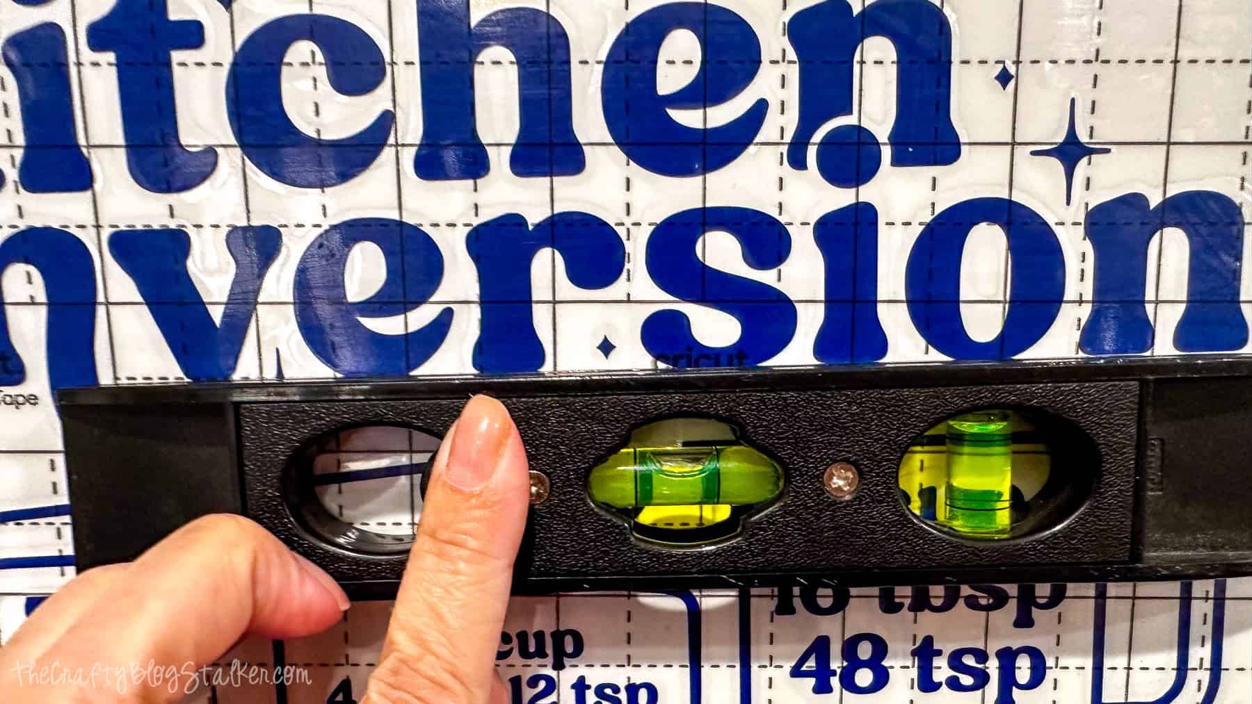 Hand holding a level tool to align a blue kitchen conversion chart vinyl decal on a wall before applying it.