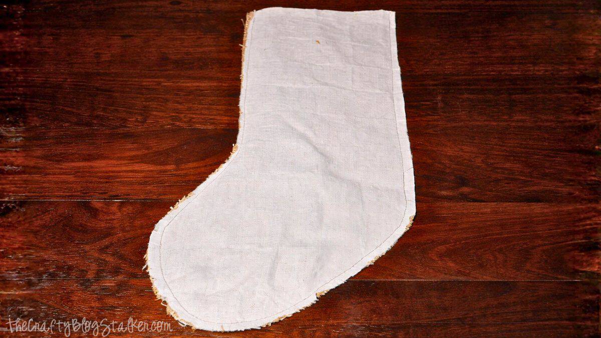 Woven Burlap Christmas Stockings Tutorial Fabric stocking shape with a sewn lining, illustrating stitched edges and seams laid flat on a wooden work surface during a DIY stocking project.
