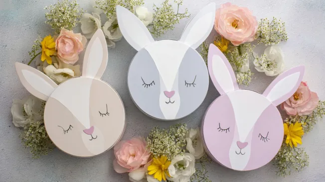 Three Easter bunny gift boxes lay beside spring flowers