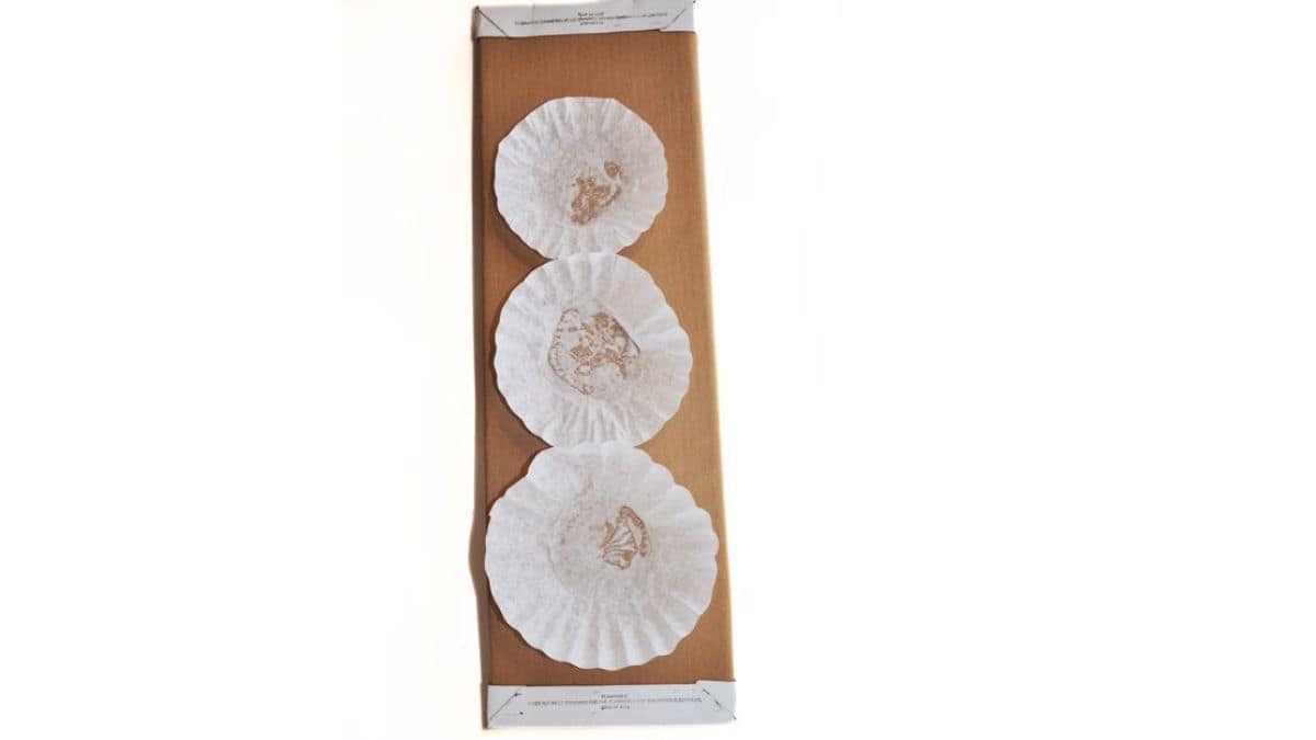 Three coffee filters affixed vertically onto a brown fabric bolt, creating the foundational shapes for a snowman craft.