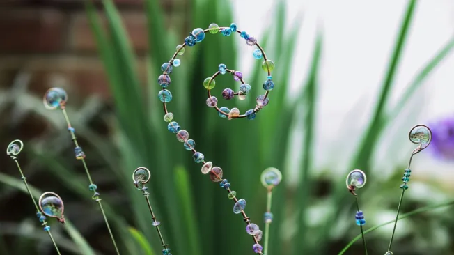 A spiral flower arrangement made of wire and beads in front of a green plant.