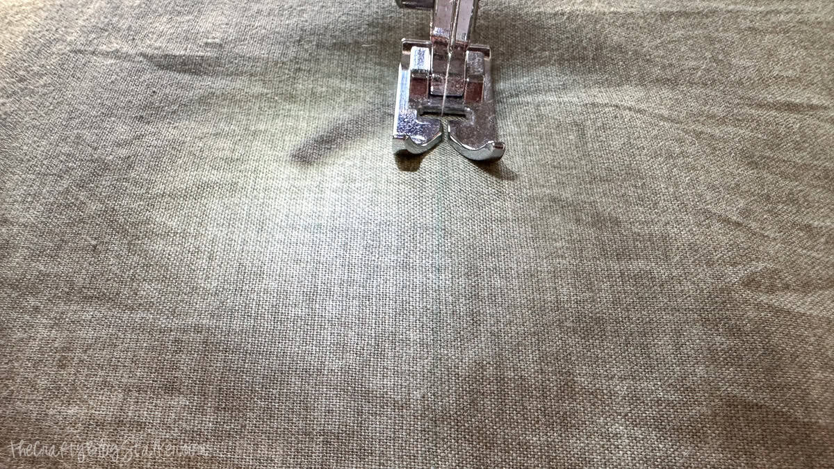 Sewing machine presser foot stitching along a marked line on green fabric to create quilting rows.