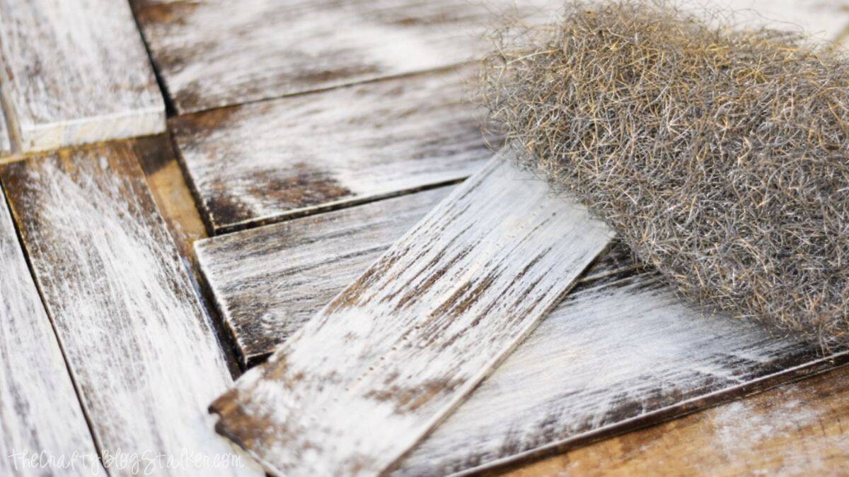 Distressed wood boards with a weathered look, displayed alongside steel wool used to achieve a rustic, aged wood texture.