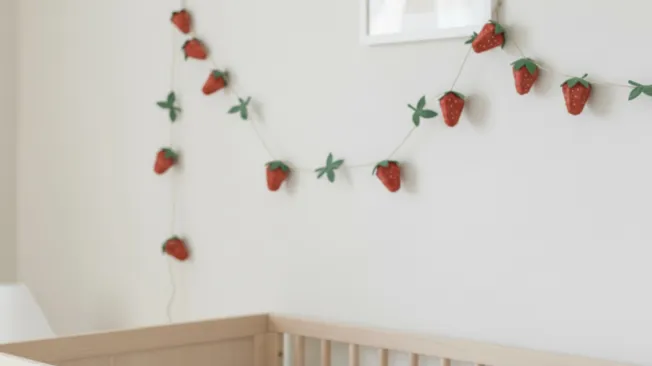 A strawberry garland made from egg cartons drapes over a crib.