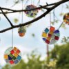 Sonnenfänger aus Heißkleber, Mosaiksteinen, Perlen und Glitzer hängen an einem Strauch