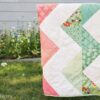 Handmade quilt with a zig zag pattern hanging outdoors on a line, featuring patchwork fabric blocks stitched together.